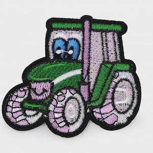 Könnte beinhalten: Gestickter Aufnäher eines Zeichentraktor. Der Traktor hat einen grünen Körper, lila und weiße Räder und blaue Augen. Der Aufnäher hat einen schwarzen Rand.