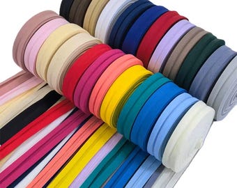 May include: A selection of colourful bias tape rolls in various shades, including pink, yellow, blue, and green. The bias tape is neatly rolled and stacked, showcasing a range of hues for sewing and crafting projects.