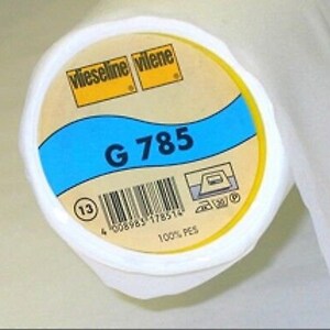 Può includere: Rotolo bianco di tessuto di interfodera Vlieseline Vilene G 785 con un'etichetta gialla e istruzioni di cura blu e bianche. L'etichetta ha un codice a barre e il testo "100% PES".