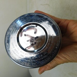 May include: A circular silver-colored metal base of a vacuum bottle with engraved text including instructions for use, capacity of thirty-two ounces, and the manufacturer name Aladdin Industries Inc., Nashville, TN, with dark markings on the center.