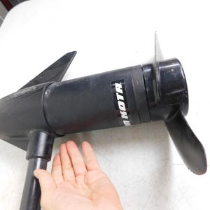 May include: Black Minn Kota boat motor with a propeller and fins. The motor is held by a hand. The motor has the brand name "Minn Kota" printed on the side.