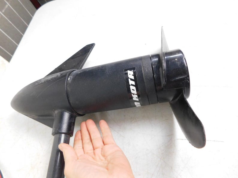 May include: Black Minn Kota boat motor with a propeller and fins. The motor is held by a hand. The motor has the brand name "Minn Kota" printed on the side.