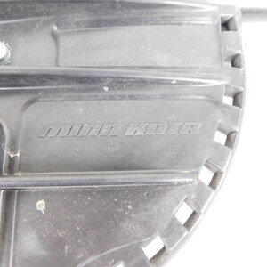 May include: Close-up of a black plastic component with the embossed text "MINN KOTA". The component has a rectangular shape with a series of square cutouts along one edge. A small circular hole is visible near the top left.