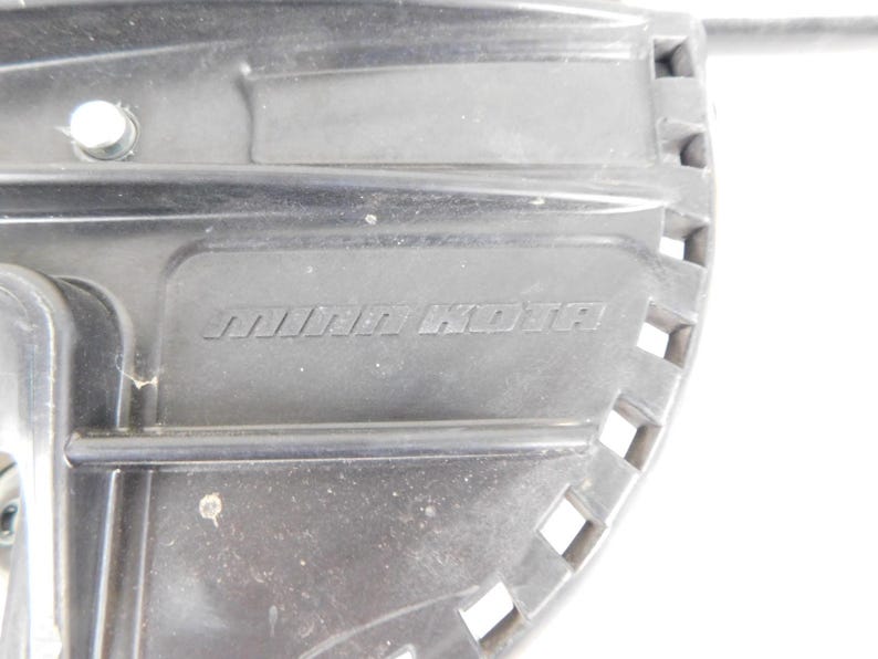 May include: Close-up of a black plastic component with the embossed text "MINN KOTA". The component has a rectangular shape with a series of square cutouts along one edge. A small circular hole is visible near the top left.