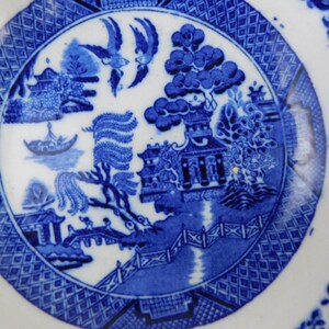 K&ouml;nnte beinhalten: Eine blau-wei&szlig;e Keramikplatte mit klassischem Willow-Muster. Die Platte zeigt eine zentrale Szene mit Br&uuml;cke, B&auml;umen und V&ouml;geln, umgeben von einem gemusterten Rand. Ein klassisches St&uuml;ck Geschirr.
