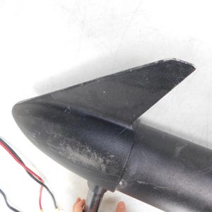 May include: A black boat motor with a fin and a cylindrical body. Red and black wires extend from the motor. The motor is set against a white background.