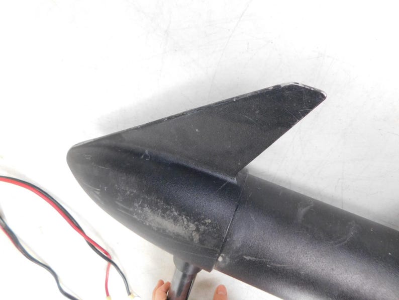 May include: A black boat motor with a fin and a cylindrical body. Red and black wires extend from the motor. The motor is set against a white background.
