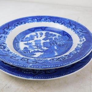 K&ouml;nnte beinhalten: Zwei blau-wei&szlig;e Keramikplatten &uuml;bereinander gestapelt. Die Teller weisen ein detailliertes, traditionelles Willow-Musterdesign mit einer zentralen Landschaftsszene und einem dekorativen Rand auf. Die Teller sind rund und haben einen wei&szlig;en Innenraum.