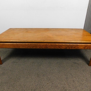 May include: A rectangular wooden coffee table with a light brown finish. The table has a simple design with four angled legs and a flat top. The wood grain is visible, adding texture to the piece.