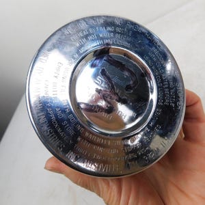 May include: A circular silver-colored metal base of a Stanley vacuum bottle. The base features embossed text including instructions for preheating and precooling, the Aladdin Industries brand name, and a capacity of thirty-two ounces.