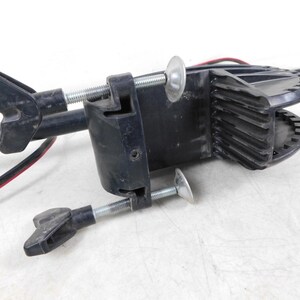May include: A black trolling motor clamp with a silver threaded rod and wing nuts. The clamp is designed to attach to a boat and hold the motor in place. Red and black wires are visible.