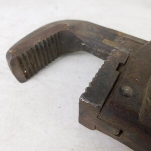 May include: Close-up of a vintage, rusty adjustable wrench. The tool is made of dark metal with visible wear and tear, showing signs of age and use. The jaws and handle have textured surfaces.