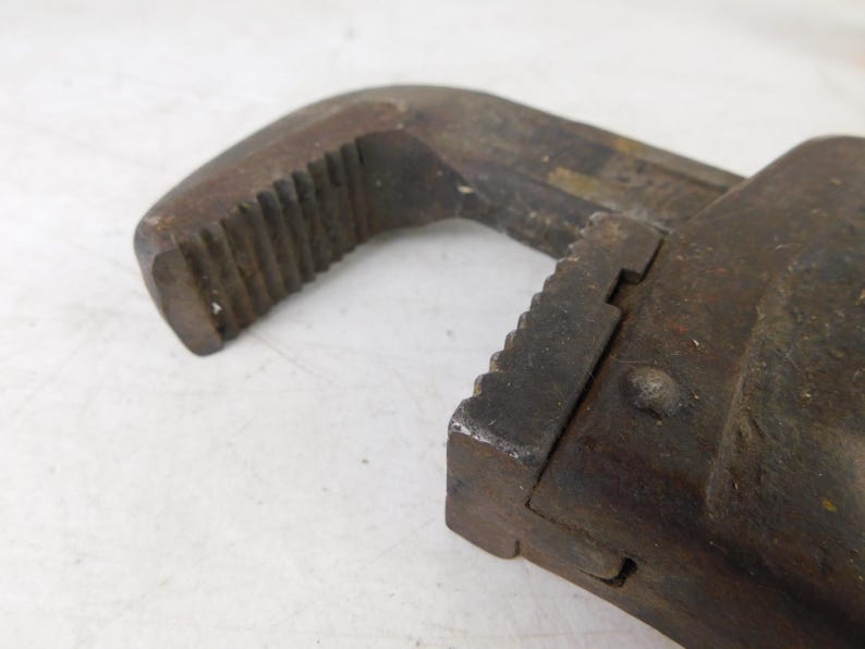 May include: Close-up of a vintage, rusty adjustable wrench. The tool is made of dark metal with visible wear and tear, showing signs of age and use. The jaws and handle have textured surfaces.