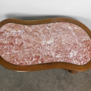May include: A kidney-shaped coffee table with a marble top and a wooden frame. The marble has a pink and white pattern. The wooden frame is a medium brown color. The table is a decorative piece.