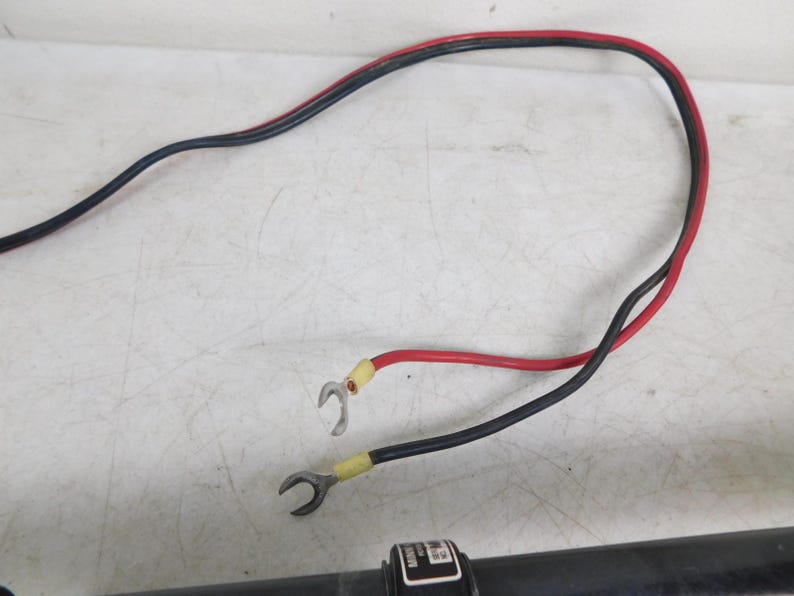 May include: A black and red electrical wire with ring terminals. The wire is curved and has a red and black sheath. The terminals are yellow and silver. The wire is on a white surface.