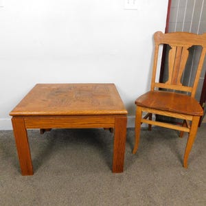 May include: A square, wooden coffee table and a wooden chair. The table is a medium brown color with a patterned top. The chair has a curved back and a seat that matches the table's color.