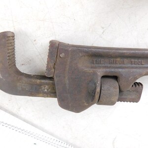 May include: A rusty, vintage pipe wrench with the text "THE RIDGE TOOL CO. ELYRIA" visible on the side. The wrench has a curved jaw and an adjustable jaw, and is likely made of steel.