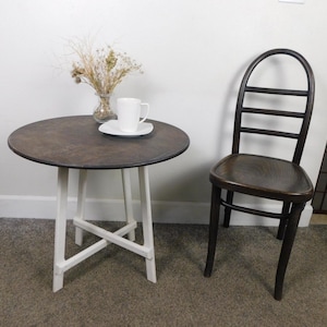 May include: A white painted round table with a dark brown wood top and a white painted X-shaped base. A dark brown wooden chair with a slatted back and a curved top sits next to the table.