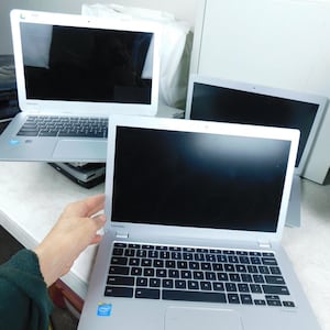 May include: Three silver Toshiba laptops with black screens and black keyboards. Each laptop features a silver chassis, a trackpad, and an Intel processor sticker on the palm rest. The devices are arranged with one in the foreground and two behind.