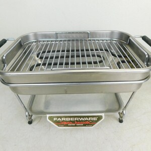 May include: A Farberware electric indoor grill with a stainless steel finish. The grill has a rectangular shape with a wire rack and black handles. The Farberware logo is visible on the front.