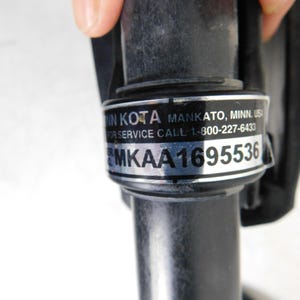 May include: Close-up of a black cylindrical component with a silver label. The label includes the text "MIN KOTA MANKATO, MINN, USA" and a service call number. The serial number "MKA1695536" is also visible.