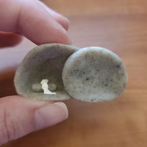 以下が含まれることがあります： 小さな灰色の粘土の洞窟の中に白い置物が入っています。洞窟は開いていて、置物は見えます。