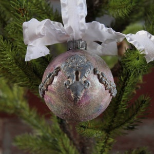 May include: A pink and silver Christmas ornament with a keyhole design and a white ribbon.