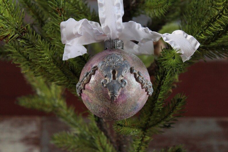 May include: A pink and silver Christmas ornament with a keyhole design and a white ribbon.