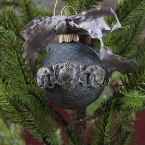 May include: A black Christmas ornament with a gold decorative band and a gray ribbon.