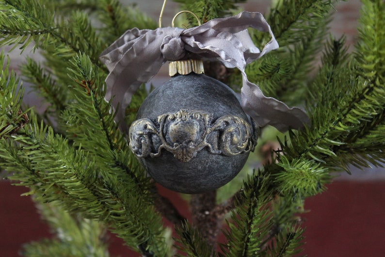May include: A black Christmas ornament with a gold decorative band and a gray ribbon.