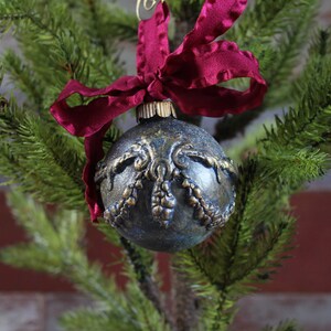 May include: A dark blue Christmas ornament with gold detailing and a burgundy ribbon.