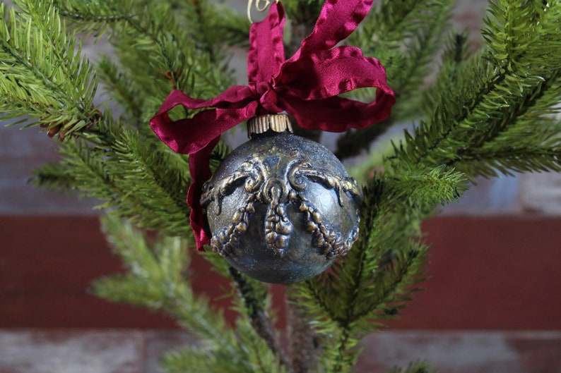 May include: A dark blue Christmas ornament with gold detailing and a burgundy ribbon.