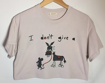 May include: A light pink cropped t-shirt with a black donkey and a small black mouse on a leash. The shirt has the text "I don't give a" printed on it.