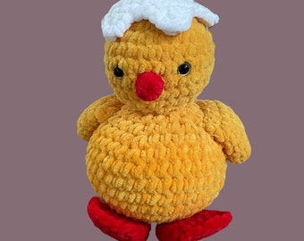 May include: A crocheted yellow chick toy with a white crocheted eggshell on its head and red crocheted feet.