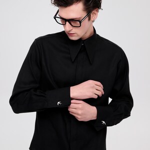 May include: A black long-sleeved shirt with a collar and a button-up front. The shirt has a small bird design on each cuff.