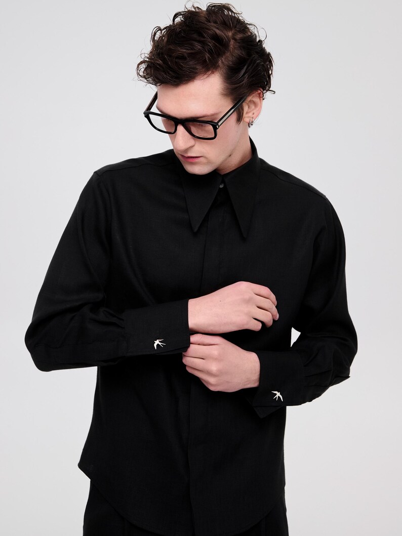 May include: A black long-sleeved shirt with a collar and a button-up front. The shirt has a small bird design on each cuff.