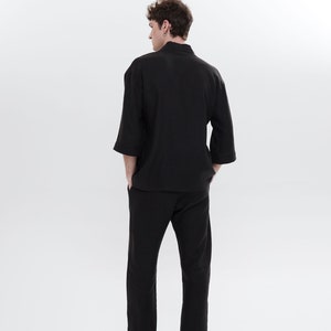 May include: A black long-sleeved shirt with a mandarin collar and matching black pants. The person is wearing black shoes.