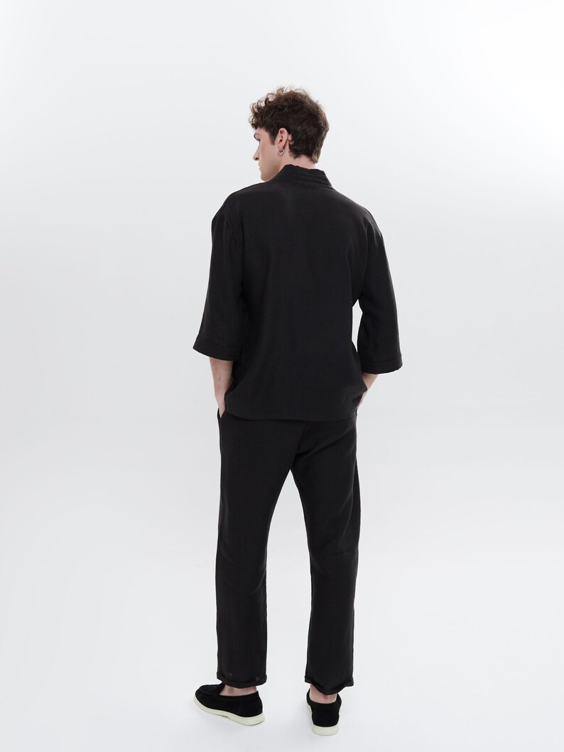 May include: A black long-sleeved shirt with a mandarin collar and matching black pants. The person is wearing black shoes.