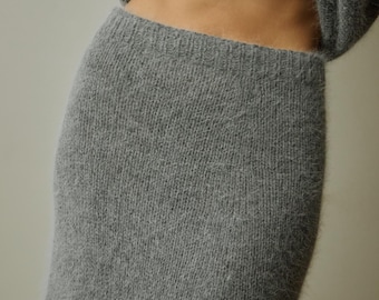 May include: A grey fuzzy knit skirt with a high-waisted elastic waistband, paired with a matching grey fuzzy knit sweater. The fabric has a soft, brushed texture throughout, creating a cohesive look with a consistent medium grey color tone.