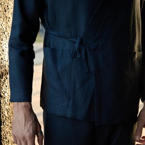 May include: Dark navy blue wrap top and matching pants. The top features long sleeves, a tie closure, and two front pockets. The outfit is made of a soft, flowing fabric, perfect for casual wear.