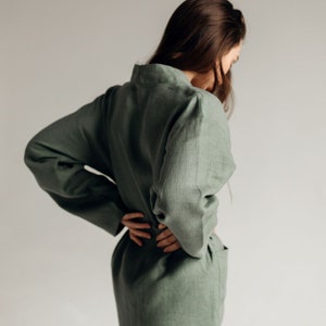 May include: A woman wearing a sage green linen jumpsuit with long sleeves and a relaxed fit.