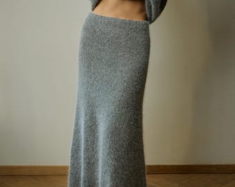 May include: A long, high-waisted, grey knitted skirt with a fuzzy, textured surface. The skirt features a straight fit that gently flares toward the hem, reaching down to the ankles. The knit material has a soft, brushed appearance throughout.