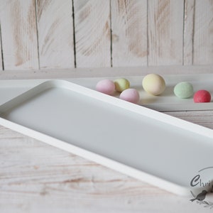 Könnte beinhalten: Zwei weiße rechteckige Tabletts, eines etwas kleiner als das andere, mit einer Vielzahl von pastellfarbenen runden Objekten auf dem größeren Tablett.