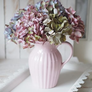 Könnte beinhalten: Ein rosa Keramik-Krug mit geriffeltem Design hält einen Strauß aus lila, blauen und grünen Hortensien.