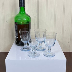 May include: A green glass bottle of wine with four clear glass wine glasses on a white platform. The glasses have a blue tint and are arranged in a semi-circle.