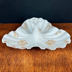 May include: A white ceramic serving dish with a scalloped edge and a floral design in gold. The dish has a central handle in the shape of a flower.