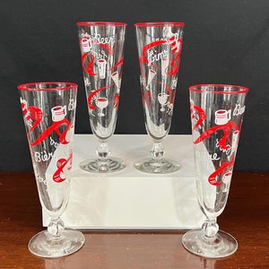 May include: Four clear glass beer glasses with red and white designs. The glasses have a red rim and a red ribbon design with the words "Beer" and "Cheers" written on them.