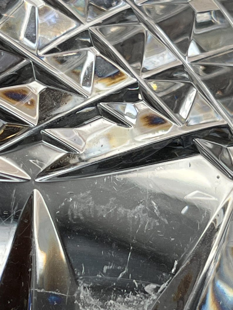 Puede incluir: Primer plano de un objeto de vidrio transparente con un patr&oacute;n geom&eacute;trico. El vidrio tiene una superficie reflectante y muestra signos de desgaste.