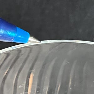 May include: Close-up of a clear glass bowl with a slightly chipped edge. The bowl has a wavy, textured surface.