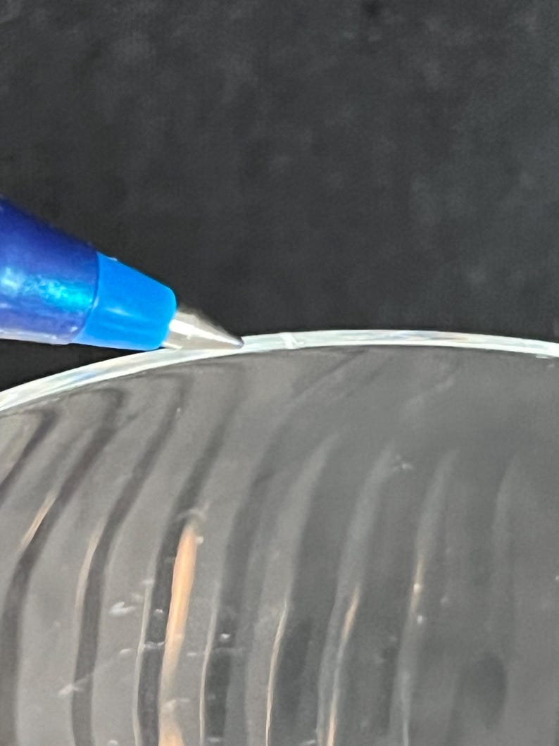 May include: Close-up of a clear glass bowl with a slightly chipped edge. The bowl has a wavy, textured surface.